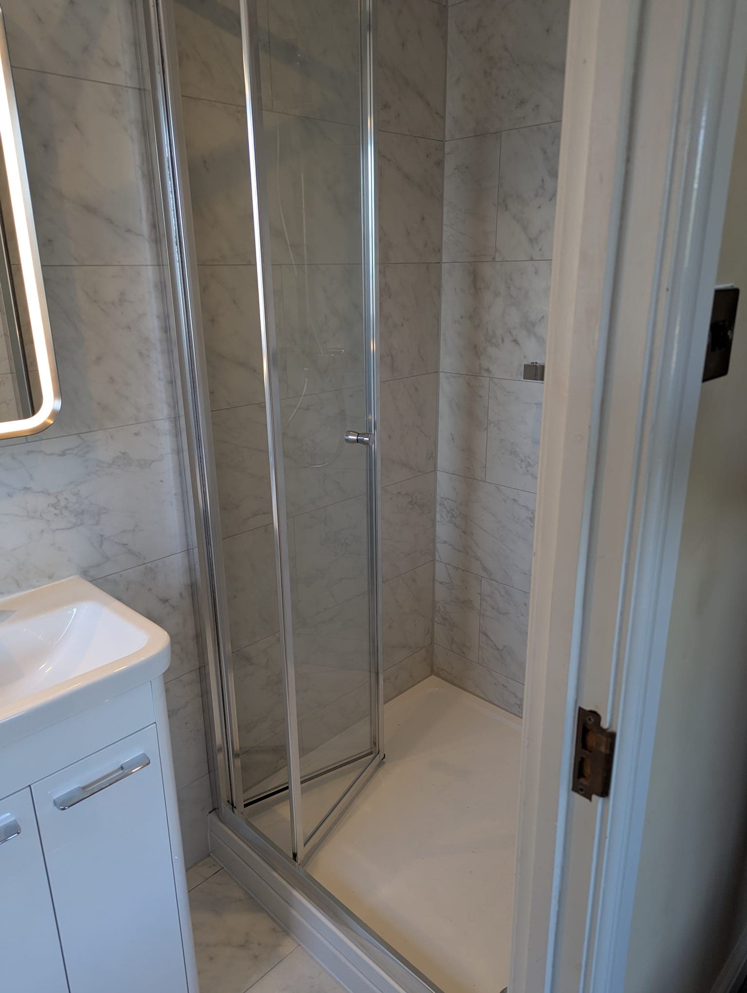Marble-effect wall tiling in a walk-in shower by Greenside Joinery